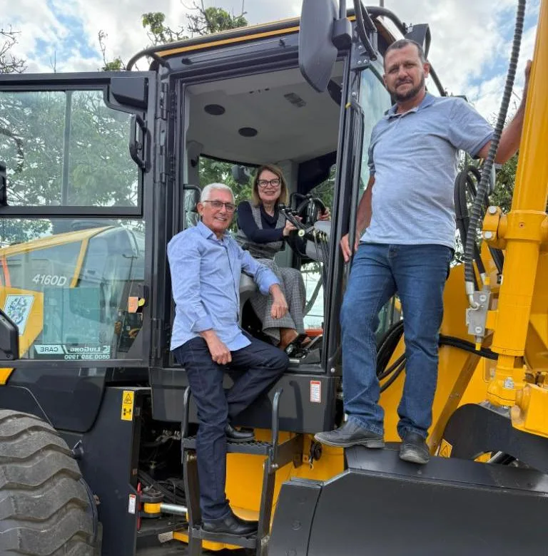 Prefeita Iracy Baltar, com o secretário de Obras Alfredo e o secretário de Agricultura Elson, posam na motoniveladora recebida por Montanha para melhorar estradas rurais.